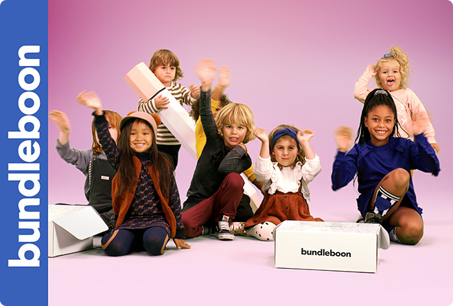 Young children pose with Bundelboon product packaging, smiling and waving in a colorful pink studio environment